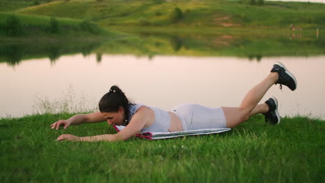 woman stretches her back and makes bends lying on the grass girl trains in the city park in nature.