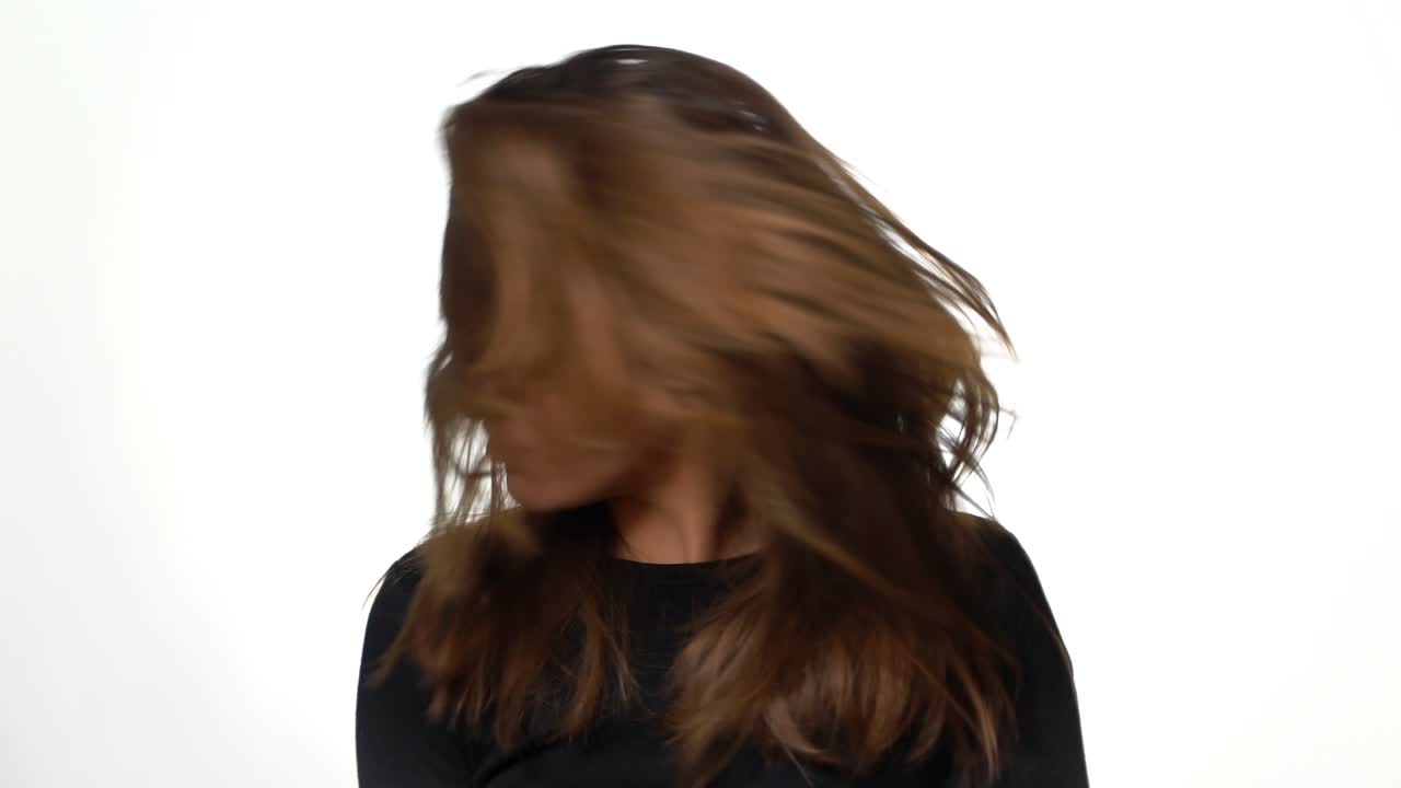 A charming girl with natural hair is waving her head to the sides on a white background in the studio. Woman is posing by her long hair
