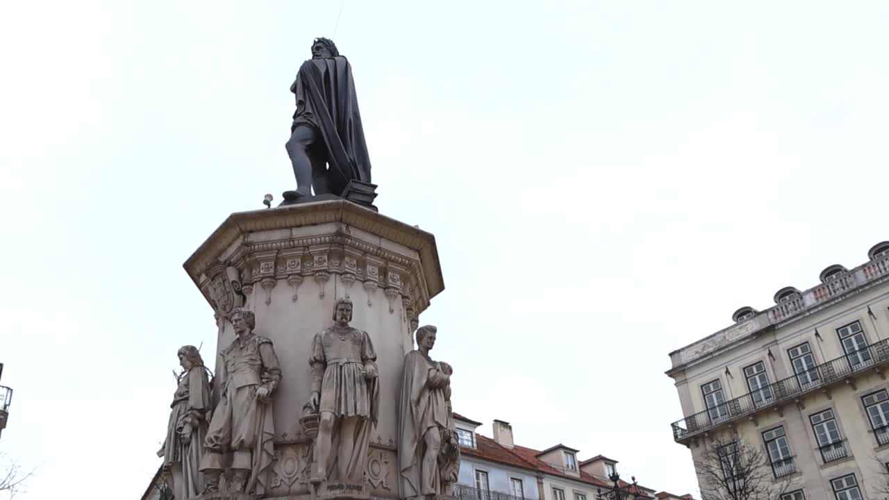 Vista dal basso del monumento a Pedro Nunes con figure in pietra ornate e l'architettura storica di Lisbona sullo sfondo.