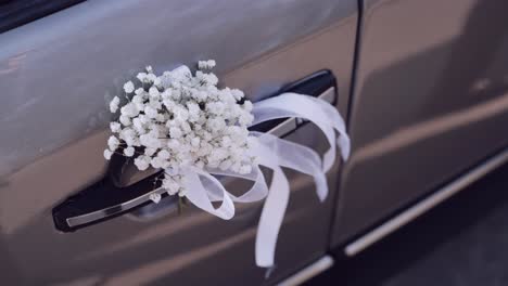 delicate white baby's breath bouquet with white ribbons on a gray car door handle