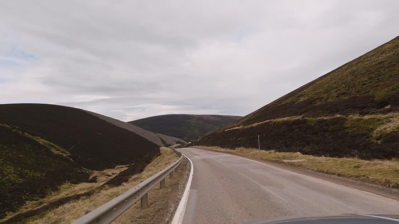 Guidando attraverso le mozzafiato Highlands scozzesi a bordo di un SUV argento, con una vista accattivante verso la lunga strada tortuosa di fronte, che rivela la bellezza aspra e lo splendore paesaggistico delle Highlands.