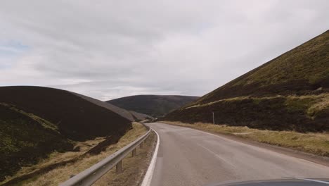 Driving-through-breathtaking-Scottish-Highlands-in-a-silver-SUV,-with-a-captivating-view-towards-the-long-winding-road-in-the-front,-exposing-the-rugged-beauty-and-scenic-splendor-of-the-highlands