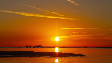 sunset over water with vibrant orange skies and silhouette of a pier, timelapse