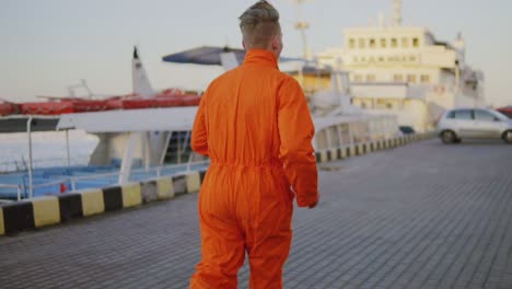 Un-Trabajador-Con-Uniforme-Naranja-Corre-En-El-Puerto.-Tiro-En-Cámara-Lenta