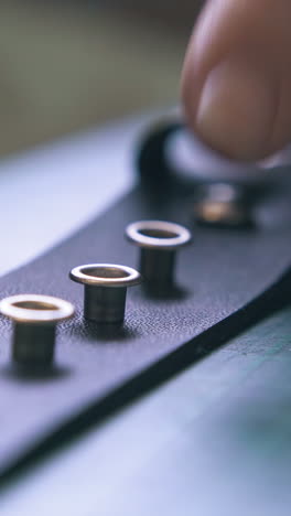 CU: Professional worker checks silver eyelets positions on stylish black leather belt in workshop close view