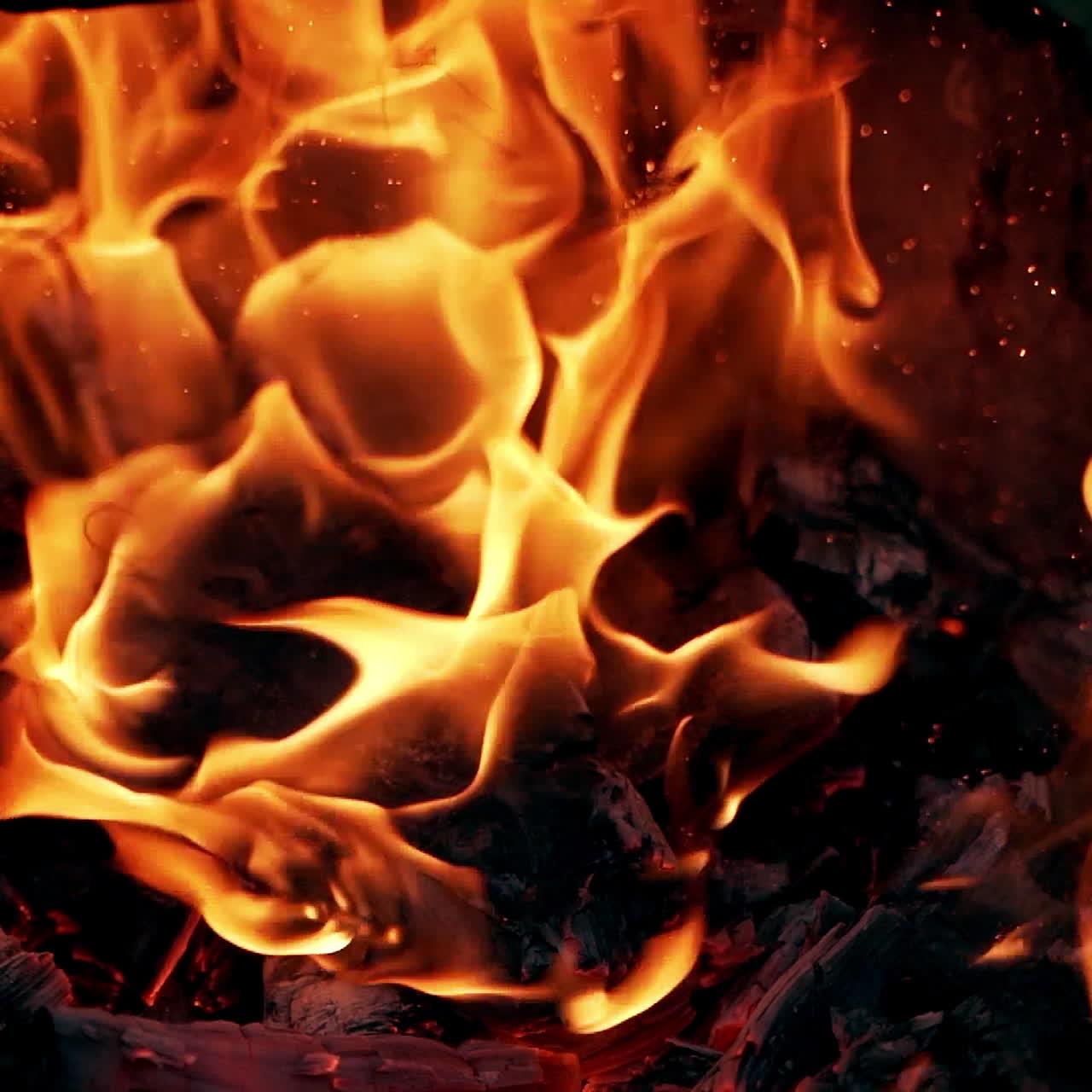 Bright fire motion. Sparkles of red and yellow flame from smoldered logs. Wooden stick beats a black log in the burning fire. Slow motion.