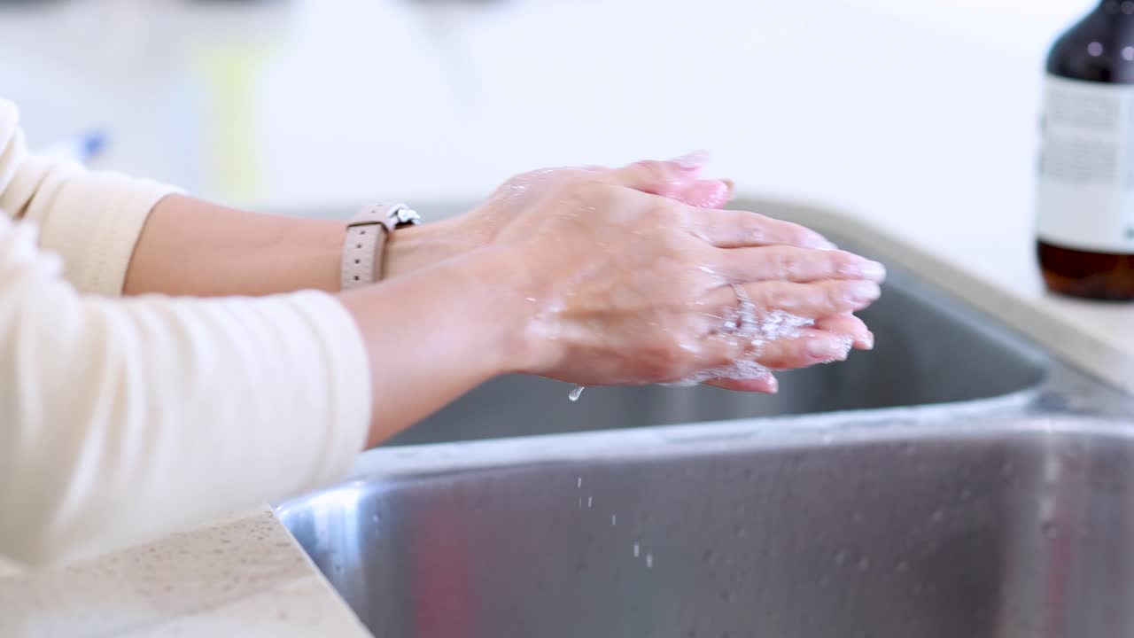 A woman thoroughly washes her hands with soap and water at a modern kitchen sink, using proper technique under bright, natural lighting with a steady camera angle