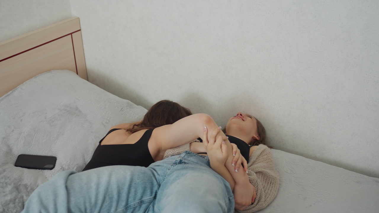 Two White Women Cuddling On Bed Sharing Laughter And Soft Embrace, Intimate Relaxed Moment With Blankets And Pillows, Affectionate Roommates Enjoying Cozy Downtime And Emotional Warmth In Private