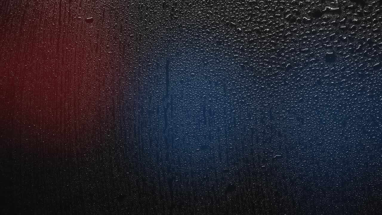 Raindrops reflecting flashing police lights at night. Raindrops on a wet surface reflect pulsating red and blue police lights at night. Atmospheric background for crime, emergency, urban drama