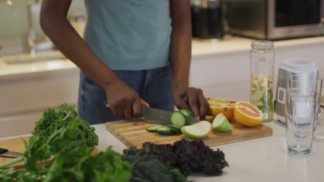 midsection of african american attractive woman chopping vegetables for smoothie in kitchen