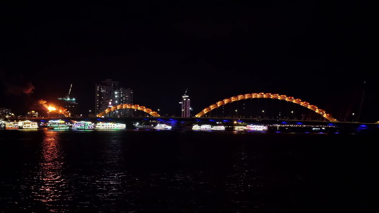 Da Nang's Dragon Bridge on the Han River spitting flames as tourists in festively lit tour boats watch.