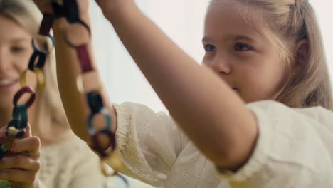 Close-up-of-caucasian-little-girl-and-mother-decorating-Christmas-tree-with-DIY-paper-chain.