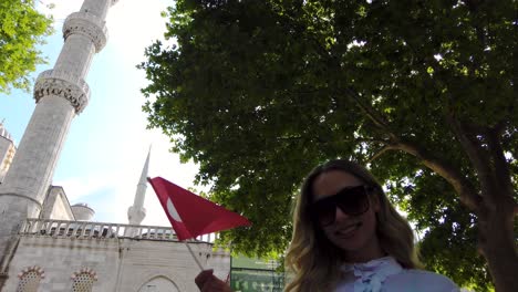 atractiva chica hermosa con camisa ondea la bandera turca con vistas a la mezquita del sultán ahmet en estambul, turquía