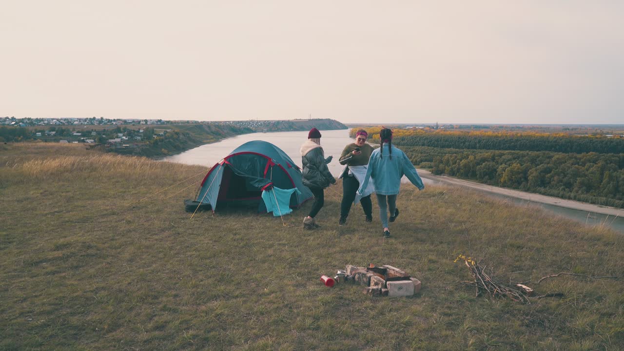여자 관광객 들 은 일몰 때 녹색 언덕 에 있는 텐트 근처 에서 춤 을 추고 있다