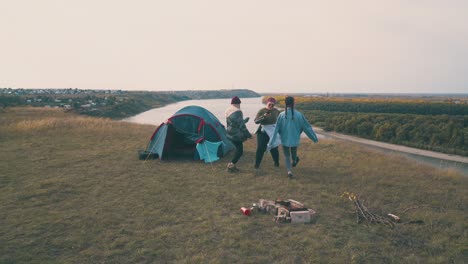 girls tourists dance near tent on green hill at sunset