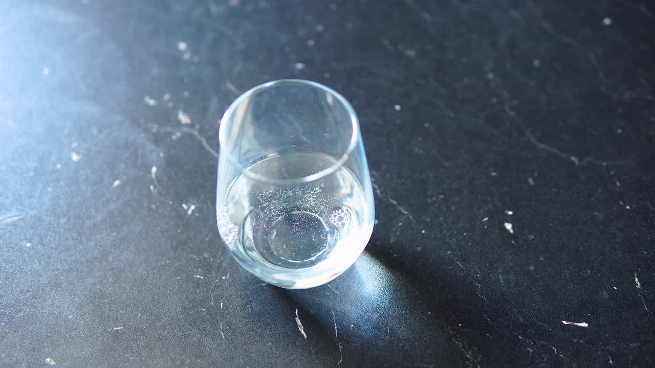 집에 있는 탁자 위에 있는 유리잔에 물을 붓고 있다