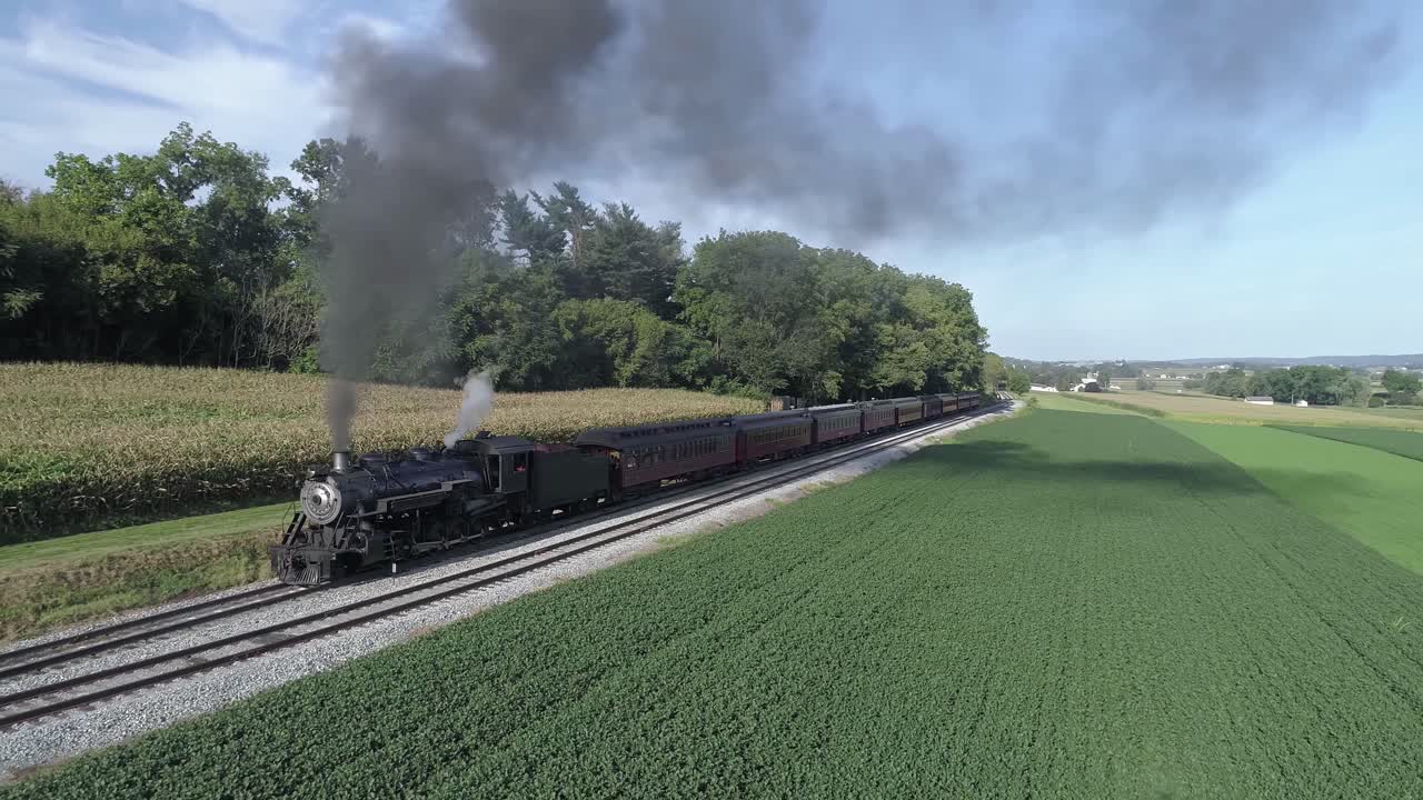 Aerial View of an Antique Restored Steam Engine Blowing Smoke with Passenger Cars pulling out of a Station on a Sunny Summer Day