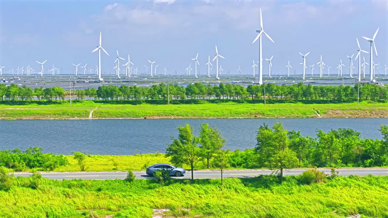 An electric car is driving outdoors, with a spinning windmill in the distance. Green new energy vehicle video
