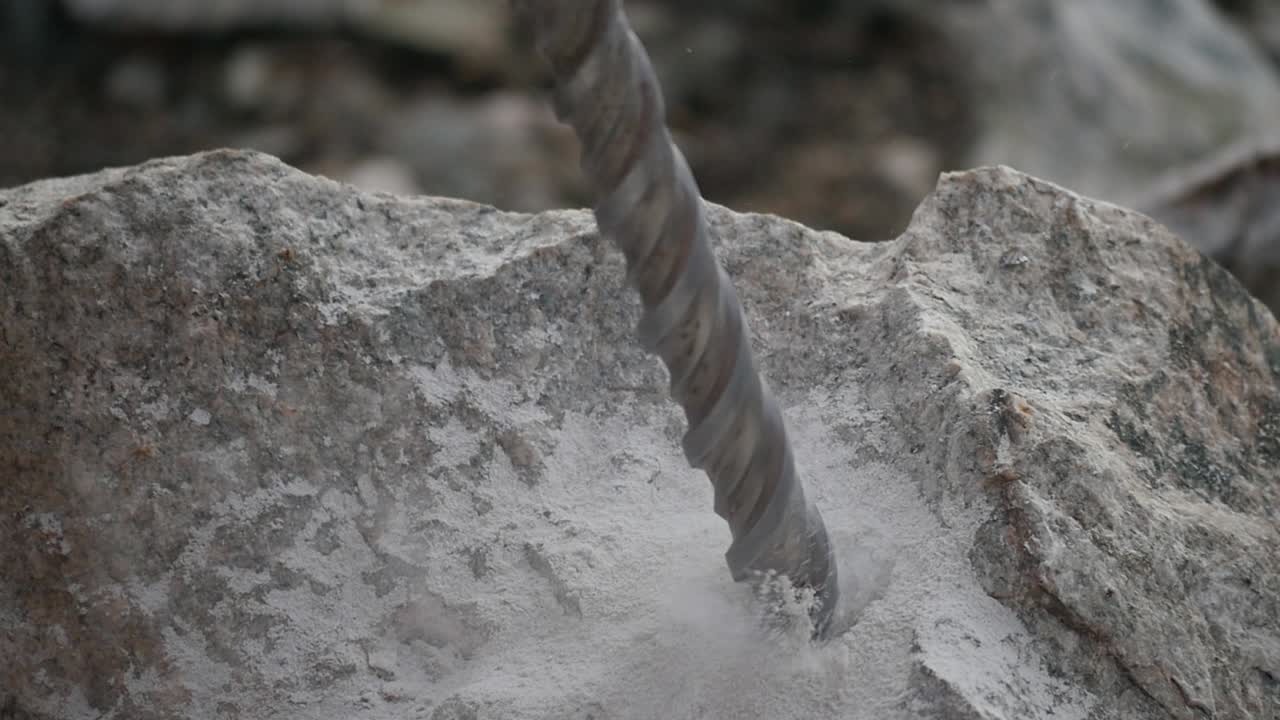 Close up of a driller digging a hole into a rock producing smoke and sand in slow motion