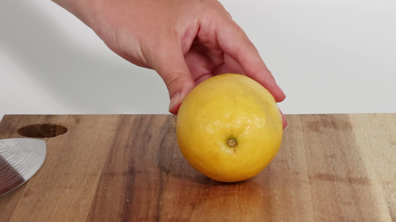 Detailed view of slicing a lemon with a knife on a wooden board, showing precise cutting technique.