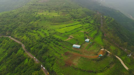 an aerial view of a ghat road in panchgani, maharashtra, shows vehicles winding through lush green mountains under a dramatic monsoon sky, capturing the season’s vibrant and misty charm 4k