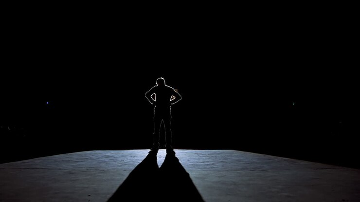 Actor man on a stage. Dark silhouette of a man wearing suit performing on a scene in theatre at spotlight. View from the stage.