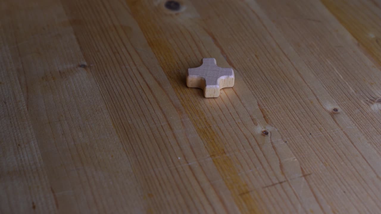 una pequeña cruz de madera se encuentra sobre una mesa de madera clara y gira lentamente a la luz