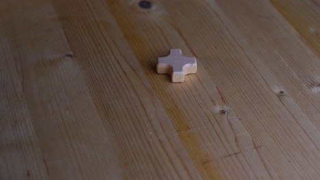 small wooden cross lies on a light wooden table and slowly rotates in the light