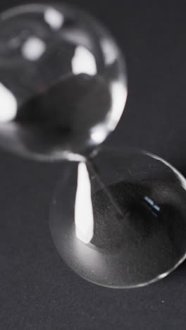 vertical video of hourglass with sand pouring, copy space on black background