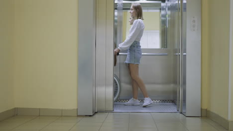 Young woman pushes button to close door of modern elevator