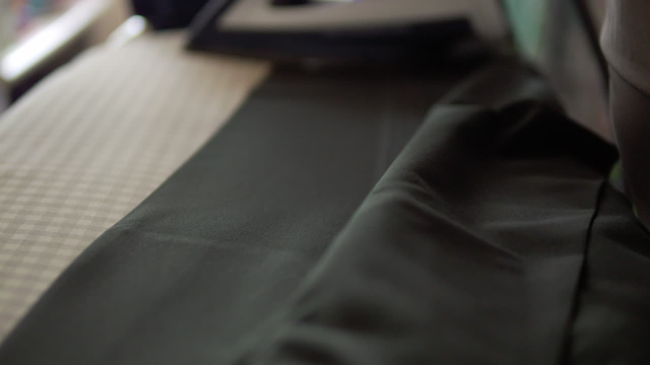 disparo de primer plano en cámara lenta de un individuo presionando un par de pantalones usando un hierro eléctrico y una tabla de planchar