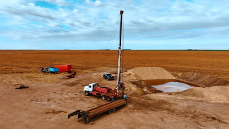 group of men stand at the truck piling the metal pipes. pool filled with water is beside the machine. yellow ripe field at backdrop.