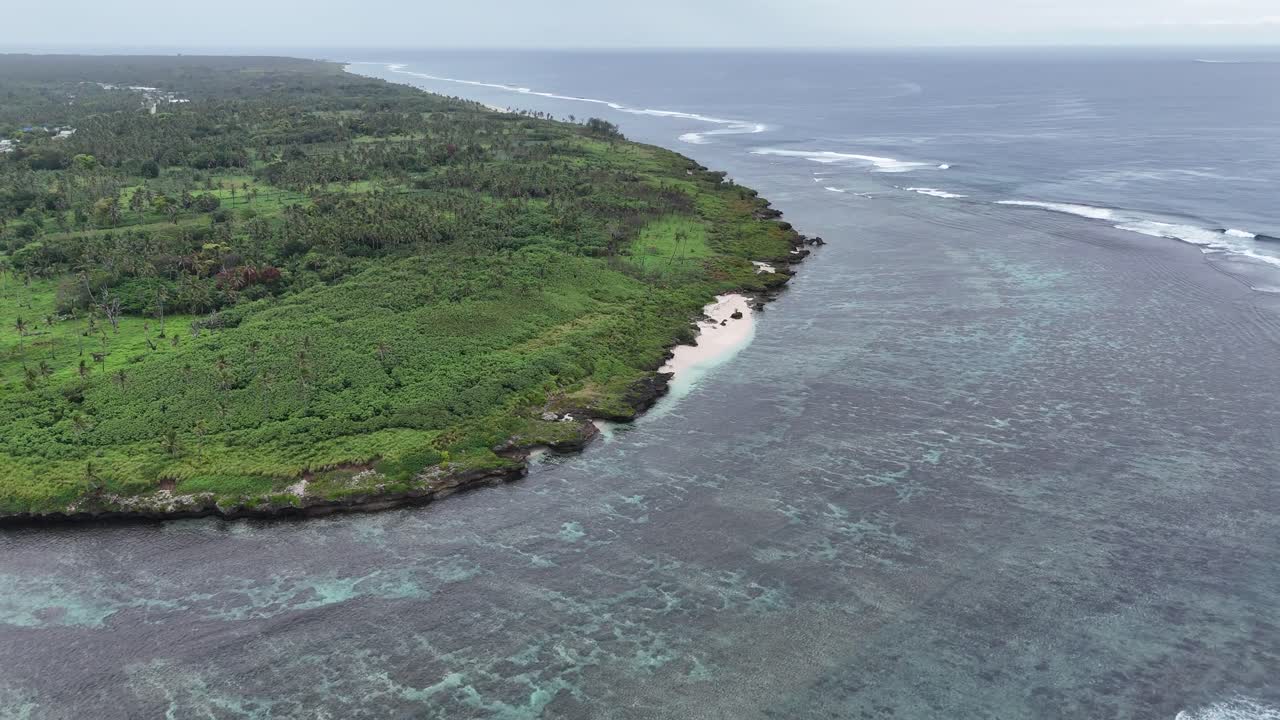 Vista aerea da drone di una remota isola tropicale a Tonga. La vegetazione verdeggiante incontra le acque turchesi incontaminate e le barriere coralline del Pacifico meridionale