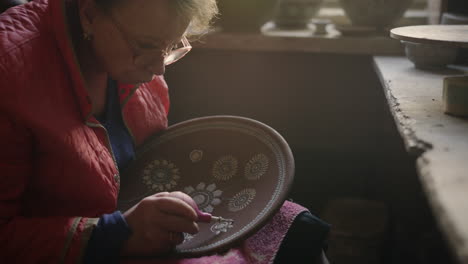 mujer mayor dibujando una placa de arcilla en cerámica. artista haciendo un ornamento en el taller