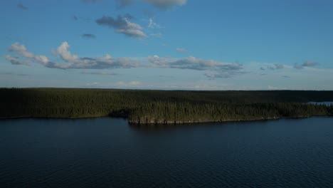 drone flying down over a wide lake on the banks of a pine tree forest
