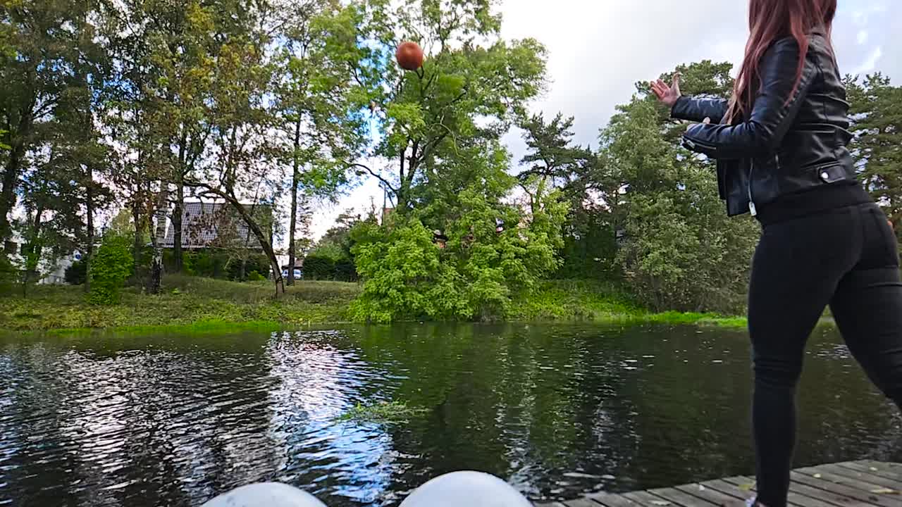 한 여성이 오렌지색 할로윈 호박을 흐르는 반사적인 강물에 던지고 물이 느리게 어지고 호박이 물속으로 가라앉는 동안 파도를 만니다.