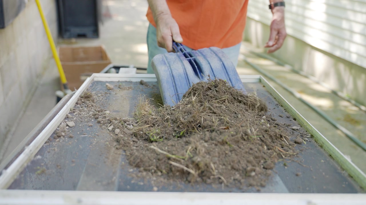 Uomo che usa una pala per setacciare il terriccio attraverso un vaglio per progetti di giardinaggio e paesaggistica