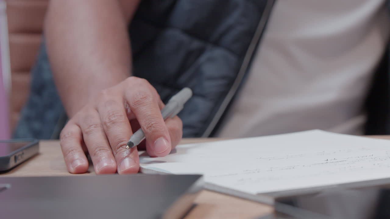 Primo piano di una mano che tiene una penna con appunti su carta durante una sessione di lavoro in ufficio