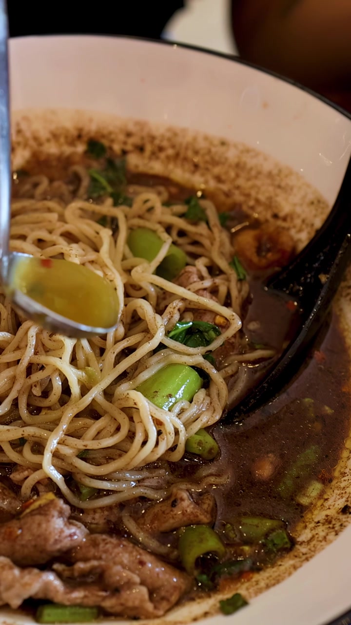 Un primo piano mostra salsa chili piccante che viene versata in una ciotola di noodles di maiale