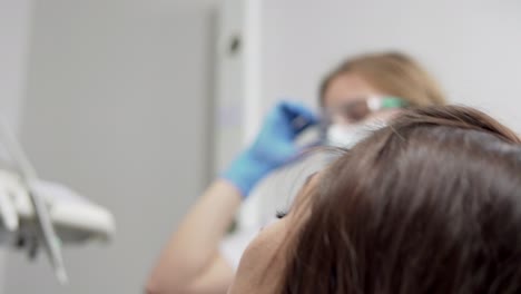 Young-female-dentist-in-gloves-and-mask-drilling-patient's-teeth-in-clinic