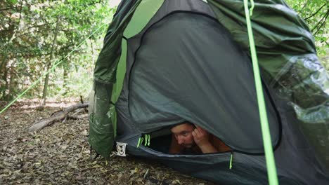 scared man unzip tent door and carefully observe surroundings in dense forest landscape