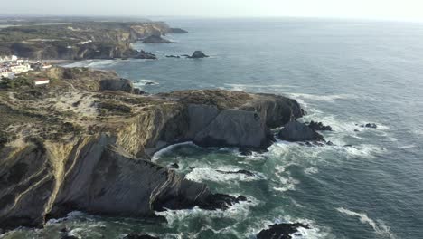 drone paning out across amazing cliffs of zambujeira, portugal with waves crashing in towards the shore