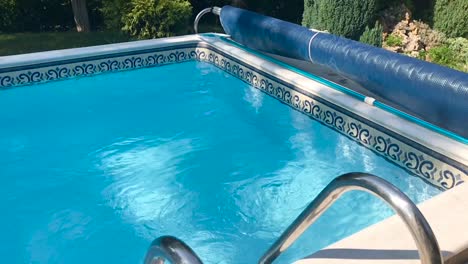 Top-view-of-scenic-open-air-crystal-clear-blue-swimming-pool-landscape-in-the-forest-with-green-plants-in-slow-motion-and-stainless-steel-pool-ladder-closeup