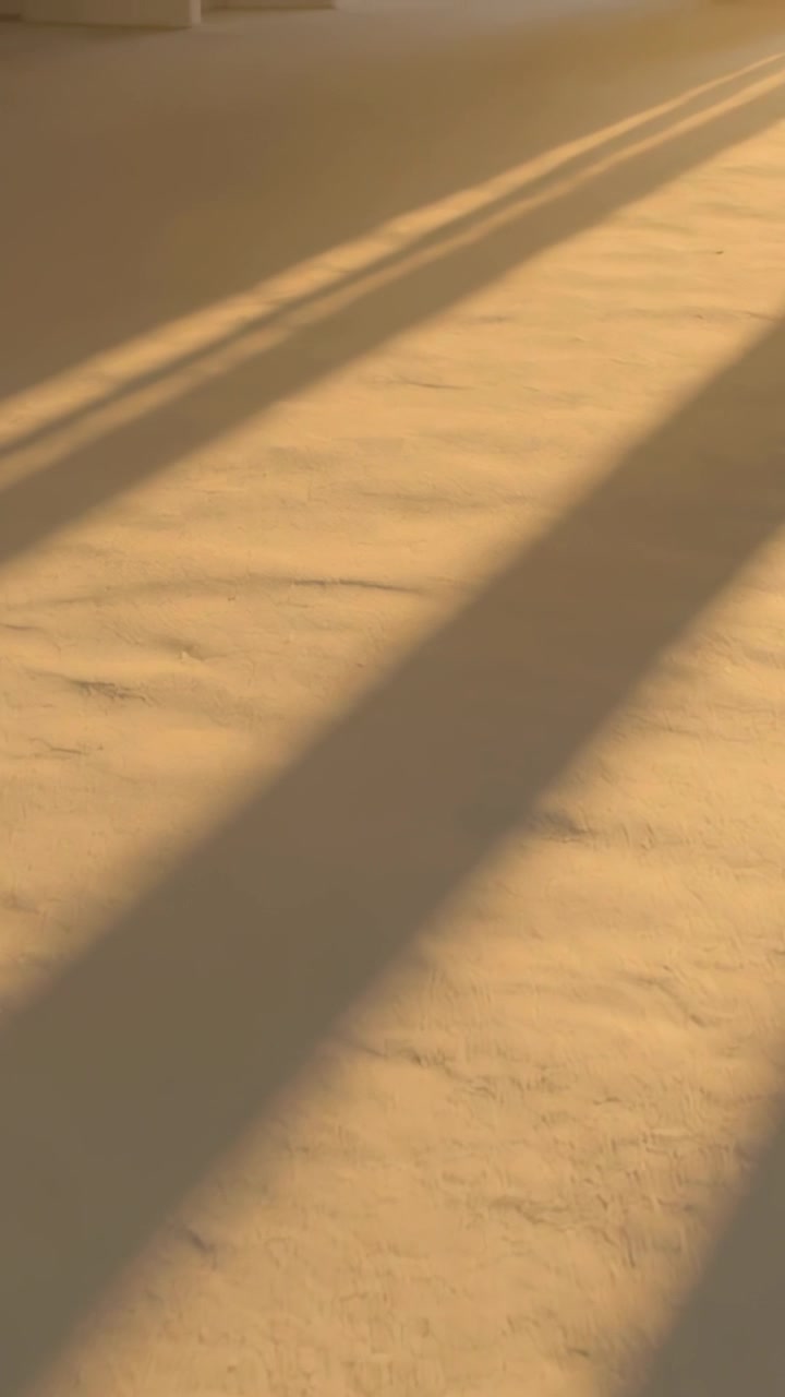 Vertical video: Shifting warm sunlight casting long shadow bands across pale textured floor indoors