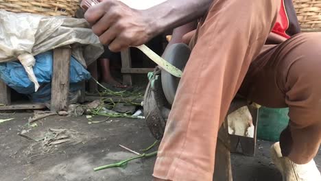 slow motion, medium shot of the hands nigerian man sharpening a knife with a rolling grinding stone