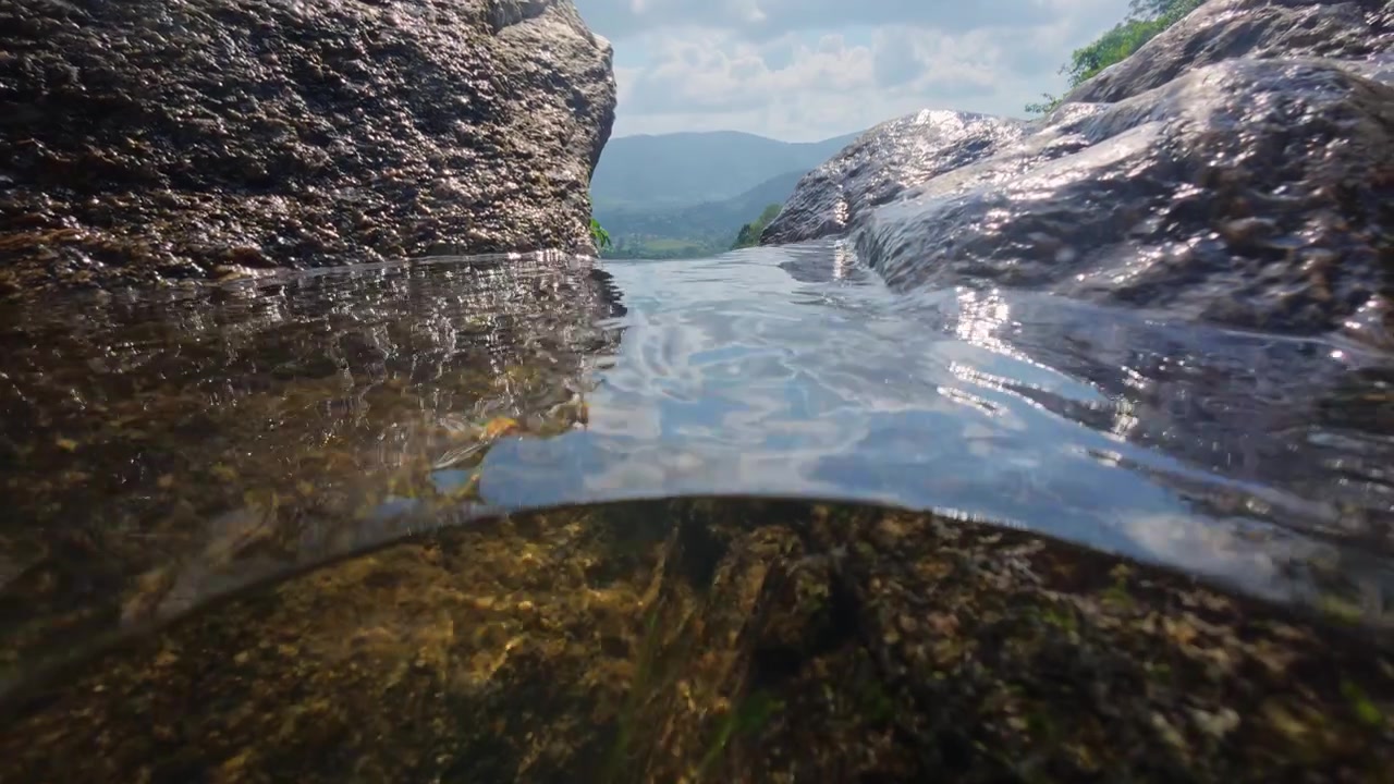 Vista da Cachoeira Na Muang 2 em Koh Samui, Tailândia, com rochas de granito molhadas, floresta tropical e paisagem montanhosa. Fotografia tirada da beira da cachoeira com água corrente em primeiro plano.