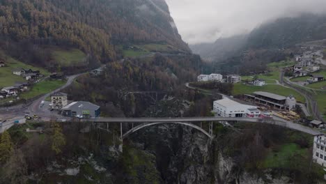 Calm-forwards-tilting-aerial-drone-view-of-Bridge-with-car-driving-over-Swiss-valley-with-pine-forests-and-clouds-on-moody-winter-day