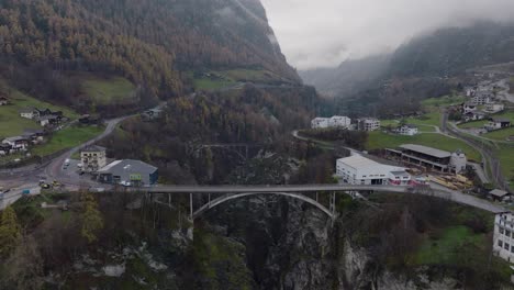 Calm forwards tilting aerial drone view of Bridge with car driving over Swiss valley with pine forests and clouds on moody winter day