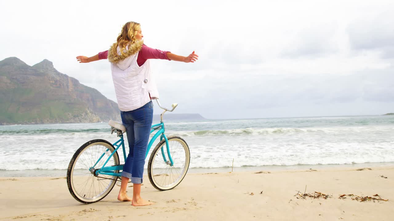 mujer de pie con su bicicleta en la playa