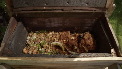 un contenedor de compostaje de madera abierto y residuos de alimentos orgánicos arrojados dentro, cámara lenta